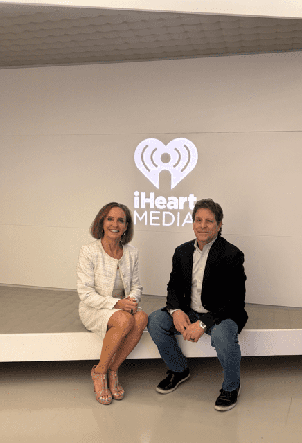 Two people seated in front of iHeartMedia logo